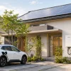 太陽光パネルと壁掛け型V2H機器が設置された戸建て住宅と白い電動SUV